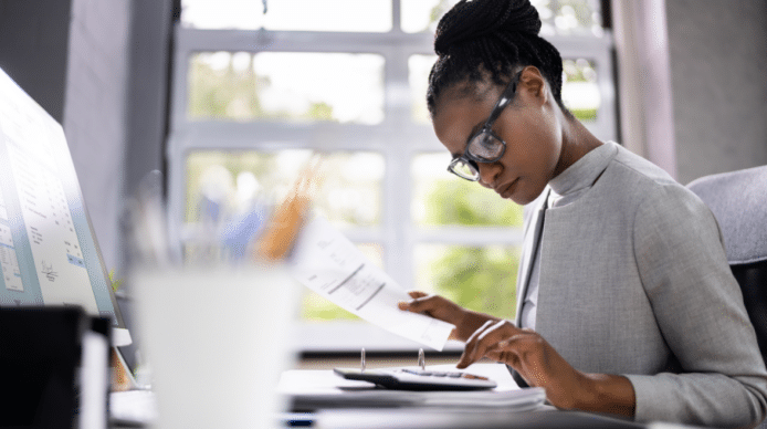 A woman wearing glasses works with a calculator while holding a financial document.